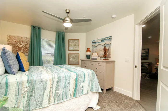 Bright and inviting bedroom featuring a cozy bed with ocean-themed bedding, elegant decor, and a sleek ceiling fan.