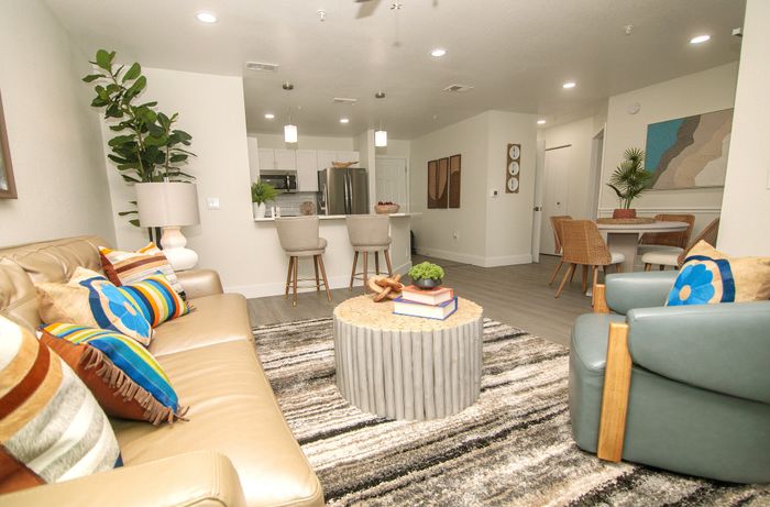 Modern open living room with cozy sofa, vibrant cushions, stylish round coffee table, and sleek kitchen bar with stools.