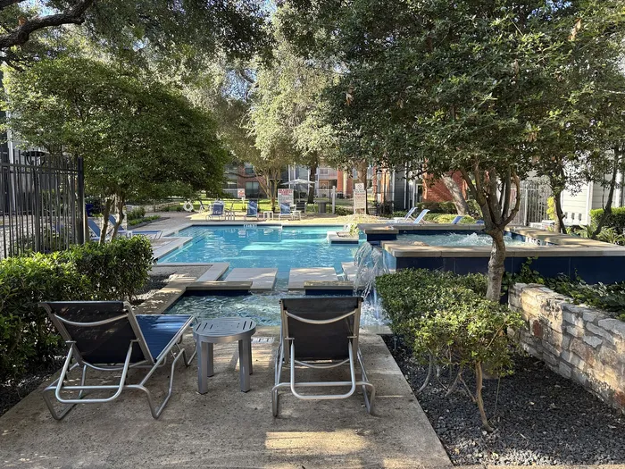 Inviting outdoor pool area surrounded by lush greenery, featuring comfortable lounge chairs and a charming waterfall for a relaxing retreat.