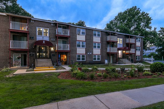 Charming brick apartment building at dusk with balconies and landscaped gardens, showcasing a welcoming and serene atmosphere.