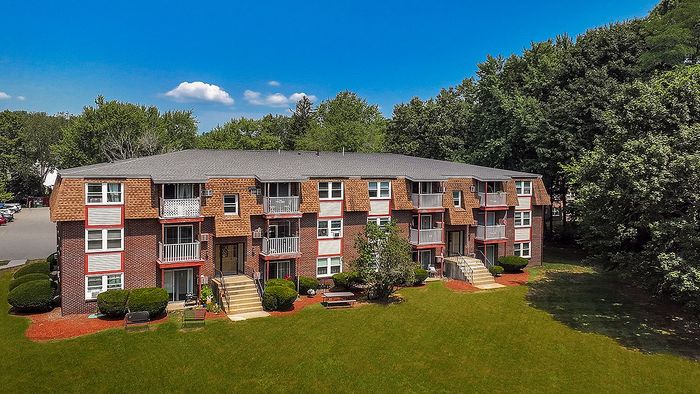 Charming brick apartment complex surrounded by lush greenery, featuring cozy balconies and inviting outdoor spaces.