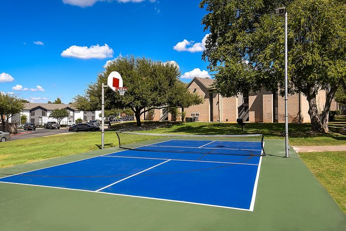 Charming apartment complex featuring a vibrant pickle ball court and basketball, surrounded by lush greenery and inviting pathways.