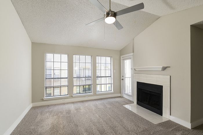 Bright living room with large windows, modern ceiling fan, and elegant fireplace, offering a cozy and inviting ambiance.