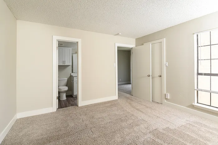 Bright and inviting bedroom with plush carpet, showcasing an en-suite bathroom and ample closet space, perfect for comfortable living.