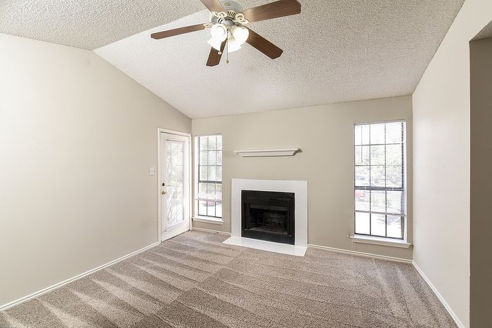 Bright and cozy living room with vaulted ceiling, ceiling fan, and charming fireplace, perfect for relaxation.