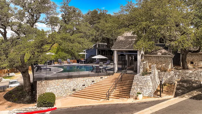 Charming residential community with a serene pool area surrounded by lush trees and a rustic stone facade.