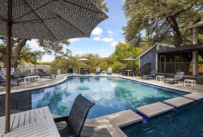 Inviting outdoor pool area surrounded by lush greenery and stylish lounging chairs, perfect for relaxing under blue skies.