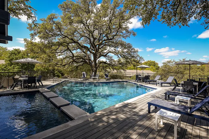 Inviting outdoor pool area surrounded by lush greenery, featuring comfortable lounge chairs and umbrella-shaded tables.