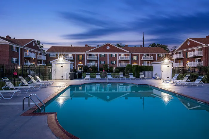 Elegant evening view of modern apartments with a sparkling pool and relaxing lounge chairs, perfect for luxury living.