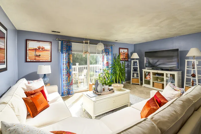 Bright and inviting living room with vibrant decor, large sectional sofa, and floor-to-ceiling windows leading to a sunny balcony.