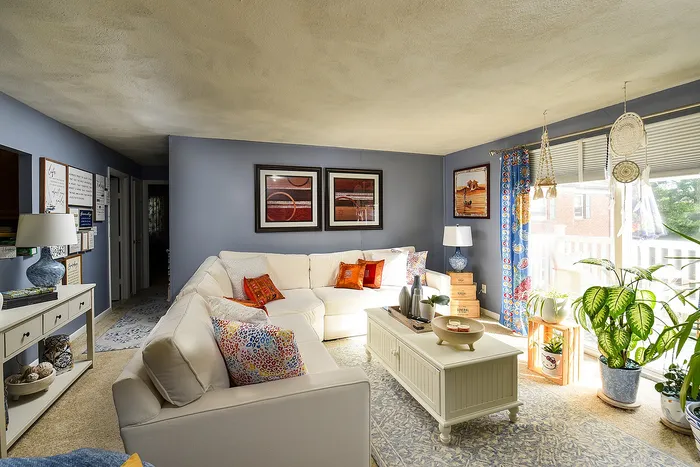Inviting living room with a cozy L-shaped sofa, colorful cushions, and vibrant decor, complemented by abundant natural light and lush green plants.