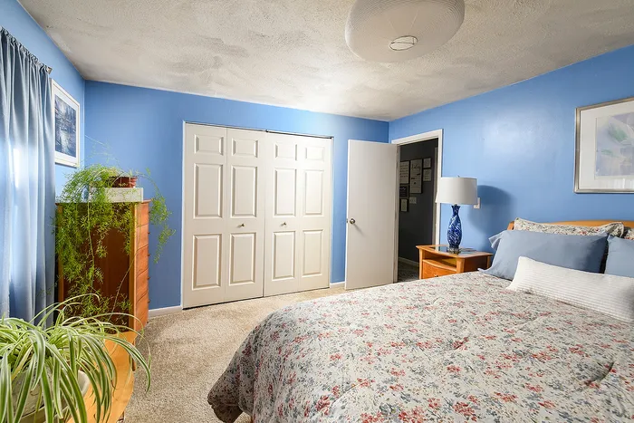 Inviting bedroom with serene blue walls, floral bedspread, and abundant natural light enhancing a cozy atmosphere.