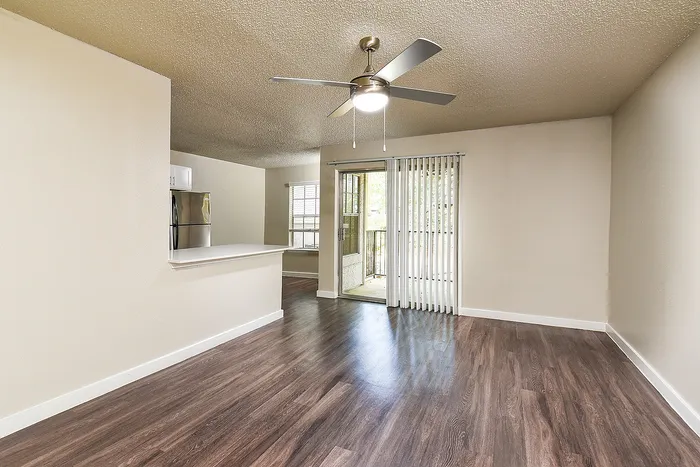 Bright and inviting living area with modern ceiling fan, open kitchen space, and laminate wood flooring, complemented by large windows and patio access for abundant natural light.
