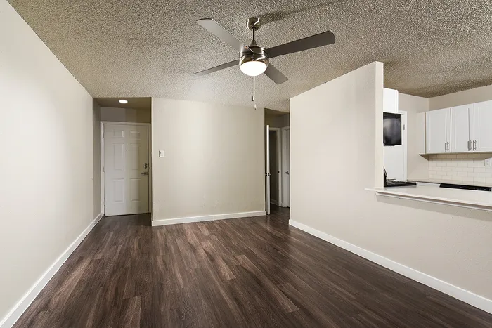 Contemporary apartment interior showcasing elegant wood flooring, a ceiling fan, and a modern open kitchen with sleek white cabinets.