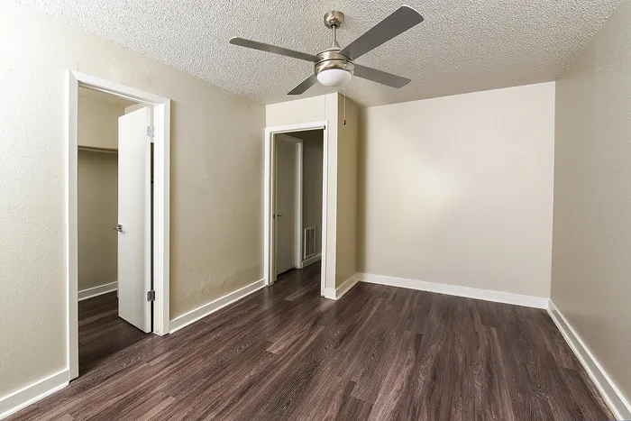 Modern bedroom with sleek wood flooring, neutral walls, and energy-efficient ceiling fan, featuring ample closet space.