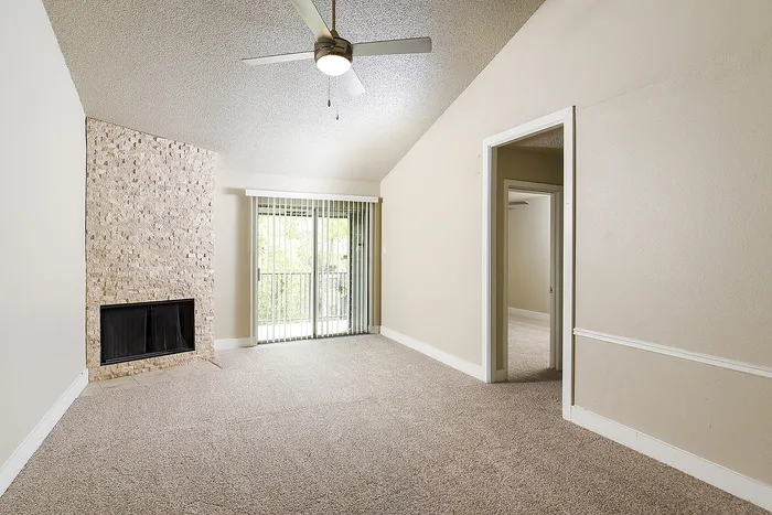 Bright living space with plush carpeting, elegant stone fireplace, and sliding glass doors leading to a vibrant garden view.