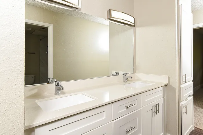 Elegant bathroom with double sinks, sleek white cabinetry, and spacious mirror under soft lighting.