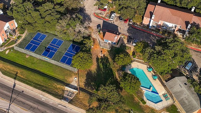 Scenic aerial view of a tranquil apartment complex featuring lush greenery, private pool, and professional tennis courts for a modern lifestyle.