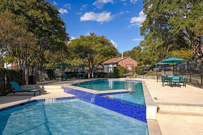 Inviting outdoor pool area with modern blue tiles, surrounded by lush greenery, lounge chairs, and shaded tables.