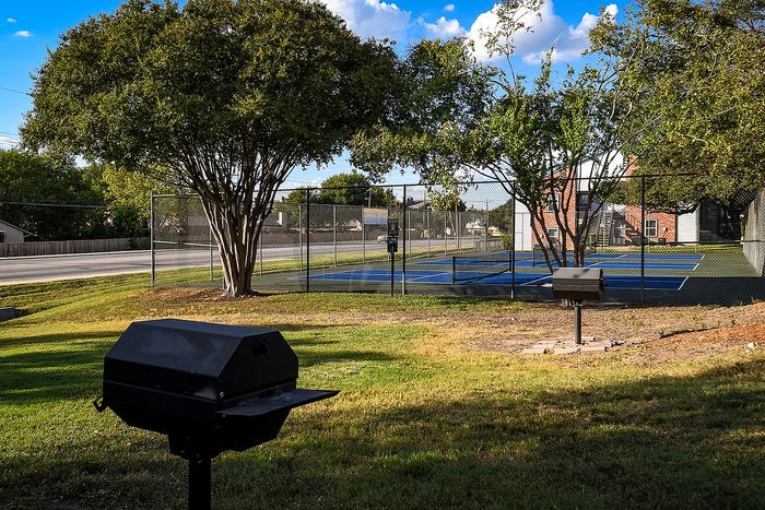 Beautiful outdoor setting with lush green space, tennis court, and convenient barbecue grills, ideal for relaxation and recreation.