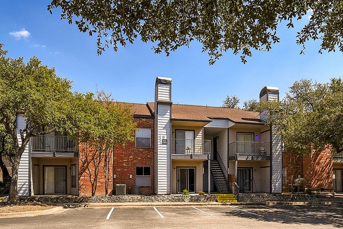 Charming two-story brick apartment building surrounded by lush greenery, offering spacious balconies and ample parking in a serene setting.