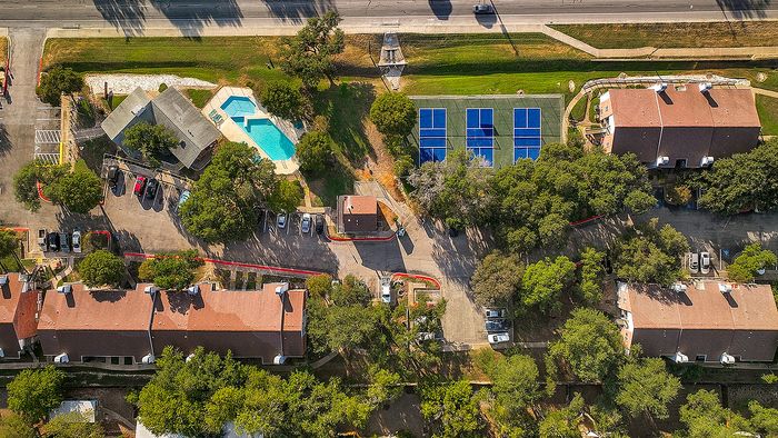 Vibrant aerial view of a residential complex showcasing manicured lawns, a sparkling swimming pool, and modern tennis courts surrounded by lush greenery.
