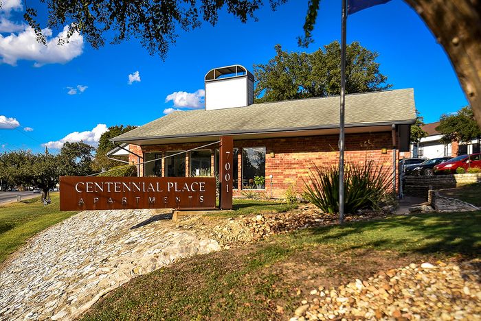 Charming Centennial Place Apartments with a welcoming facade set amidst lush greenery and a bright blue sky.