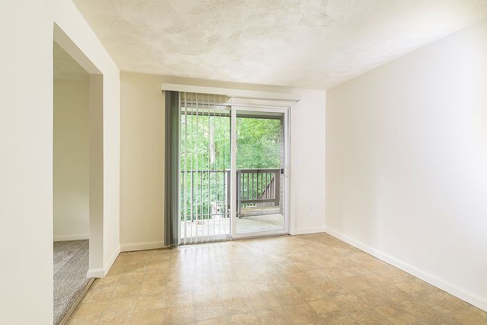 Bright apartment interior with elegant flooring and expansive sliding glass doors opening to a private balcony with lush green views.