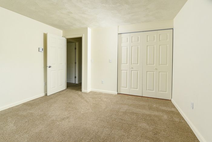 Bright and spacious bedroom with plush carpeting, featuring double doors to ample closet space and an inviting entrance.