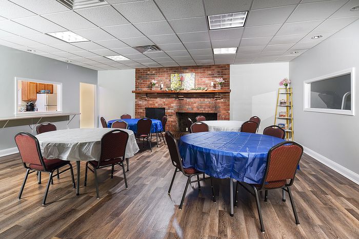 Charming communal room featuring elegant round tables, cozy brick fireplace, and vibrant decor for a welcoming atmosphere.