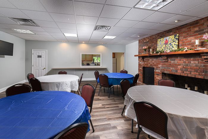 Inviting community room with vibrant blue and white table settings, a cozy brick fireplace, and modern lighting, perfect for social gatherings.