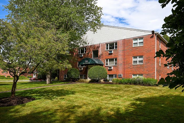 Charming brick apartment building with lush green landscaping and elegant entrance canopy.