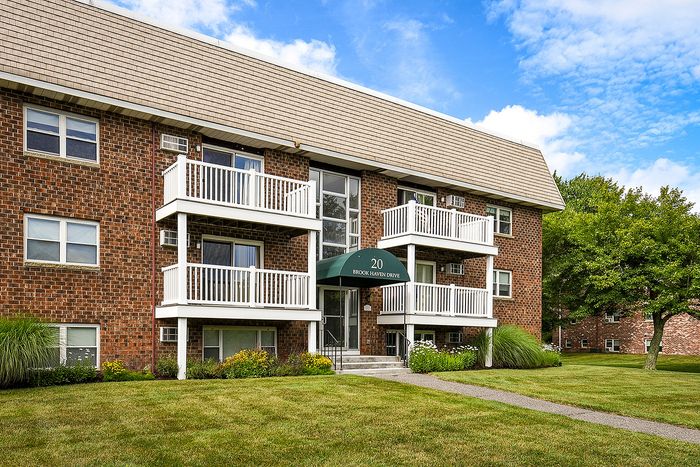 Charming brick apartment building with white balconies, surrounded by lush green lawn and trees, offering serene residential living.