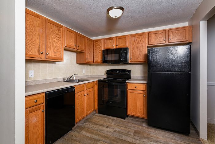 Modern kitchen with sleek black appliances, warm wooden cabinets, and elegant tile backsplash.