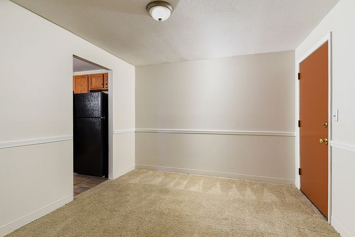 Cozy apartment entryway with plush carpeting, leading to a modern kitchen with sleek black appliances.