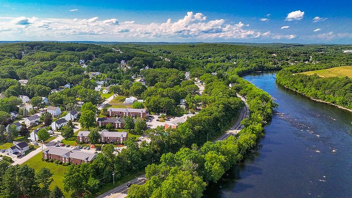 Charming aerial view of a riverside community surrounded by lush greenery and vibrant homes, offering a tranquil living experience.