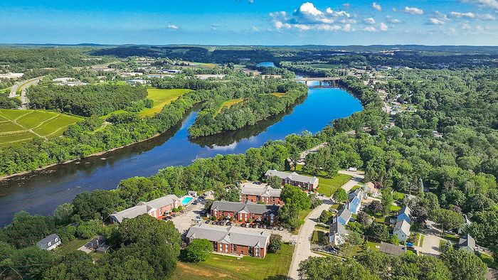 Captivating aerial view of a vibrant residential community nestled along a serene, tree-lined river, with scenic landscape and lush greenery.