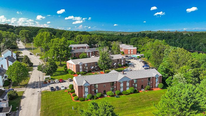 Charming aerial view of a serene apartment complex surrounded by lush greenery and open skies.