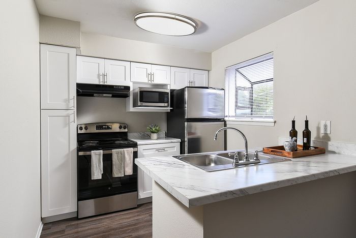 Modern kitchen featuring sleek stainless steel appliances, white cabinetry, and elegant marble countertops with a cozy breakfast bar.