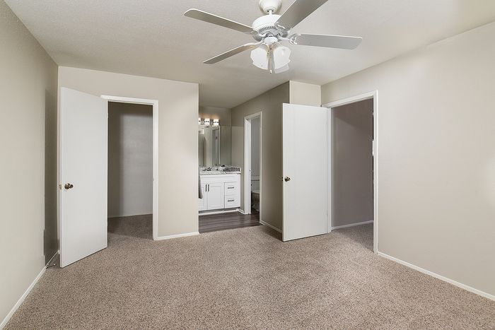 Bright and airy bedroom with soft carpeting, featuring a ceiling fan and en-suite bathroom for ultimate comfort.