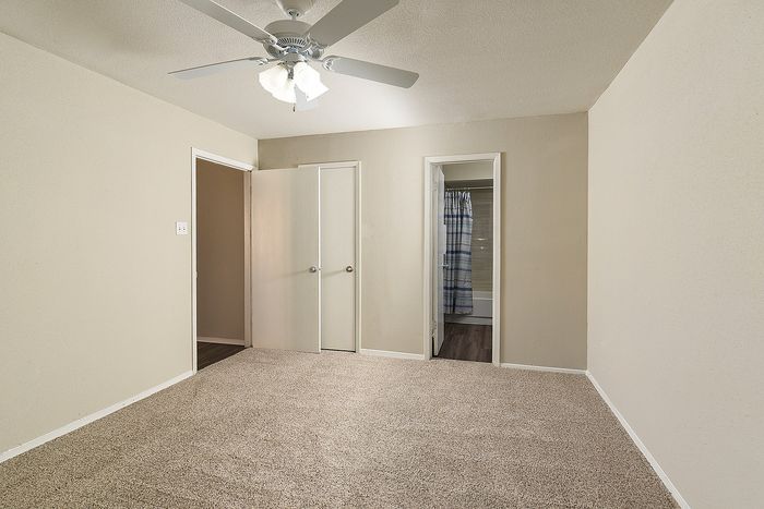 Bright and spacious bedroom with plush carpeting and modern ceiling fan, featuring large closet and adjacent bathroom for convenience.