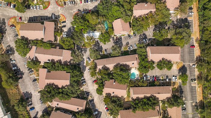 Scenic aerial view of a charming residential complex surrounded by lush greenery, featuring ample parking and a refreshing central pool.
