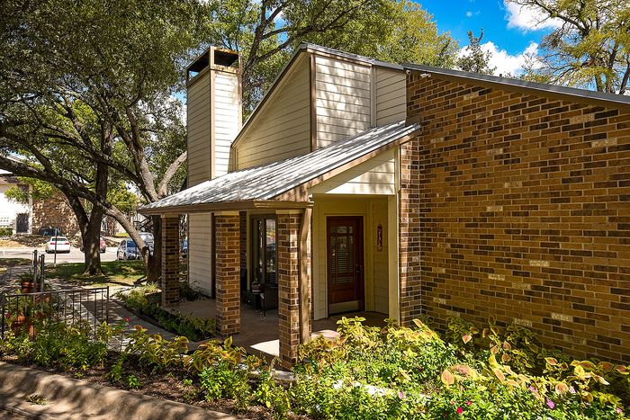 Charming brick townhouse with inviting porch surrounded by lush greenery, nestled under mature oak trees.