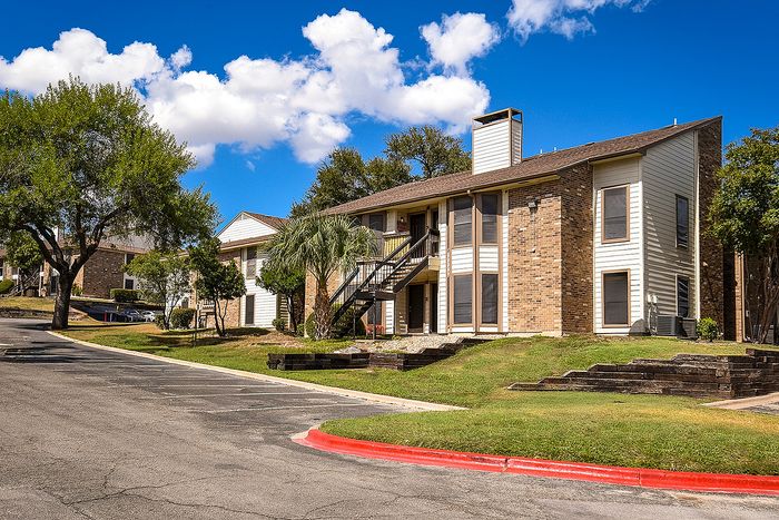 Charming two-story brick apartment building with lush greenery and a serene residential setting under a vibrant blue sky.
