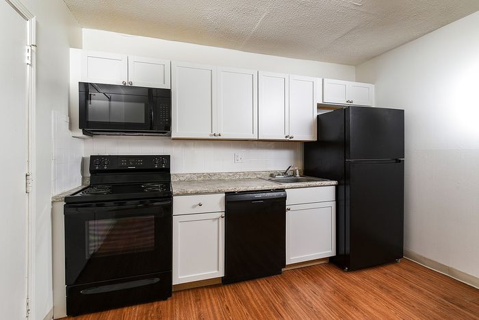Modern kitchen with sleek black appliances, white cabinetry, and wood flooring, offering a clean and stylish cooking space.