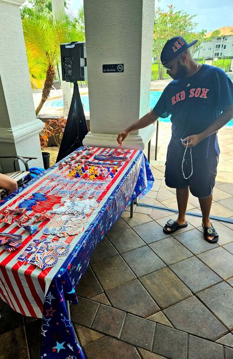 Festive outdoor setup with vibrant red, white, and blue decorations by the poolside, featuring a person selecting patriotic-themed party favors.