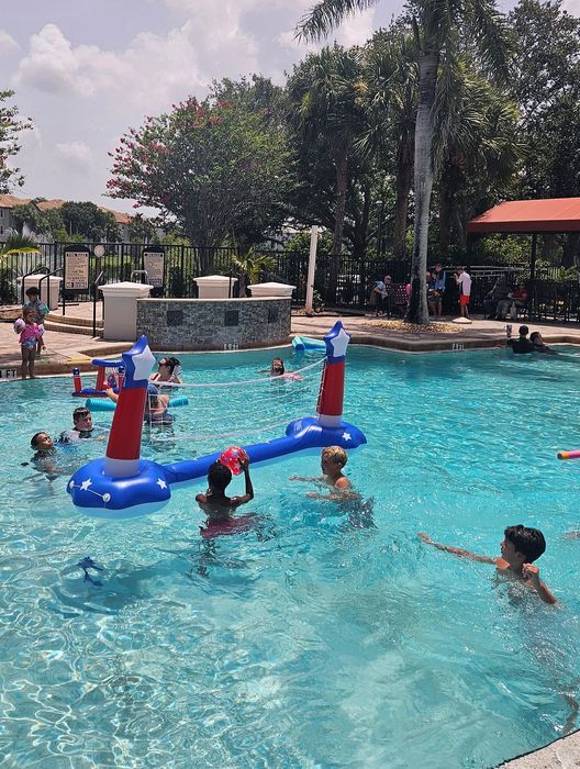 Vibrant community pool area featuring a refreshing swimming pool with playful inflatable volleyball game, surrounded by lush greenery and outdoor seating.
