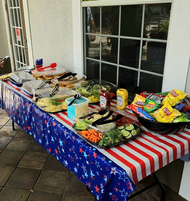 Vibrant outdoor buffet with colorful star-themed tablecloth, offering a variety of fresh vegetables, condiments, and an assortment of chips.