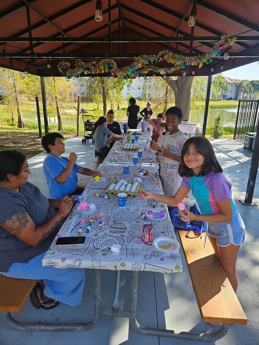 Joyful outdoor gathering under a decorated gazebo with families and children crafting unique art pieces on a sunny day.