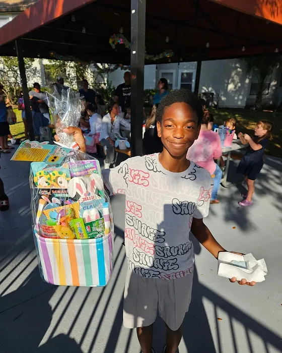 Cheerful gathering outdoors with a young person holding a colorful gift basket, bringing joy to a lively community event.